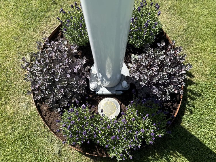Rund bedring i cortenstål omkring flagstang med blomster