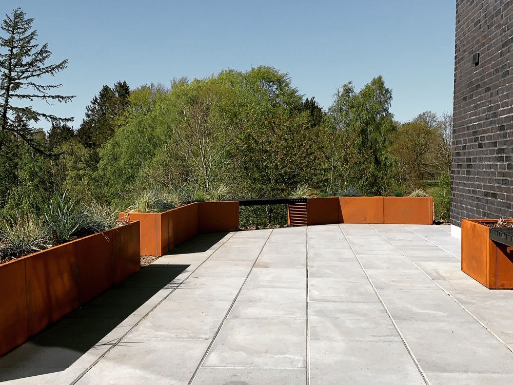 Lang række byJEMA plantekasser i cortenstål langs terrasse i moderne have