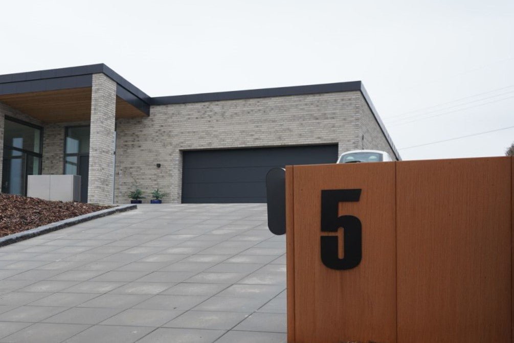 Skraldespandsskjuler i cortenstål med sort husnummer monteret i indkørsel