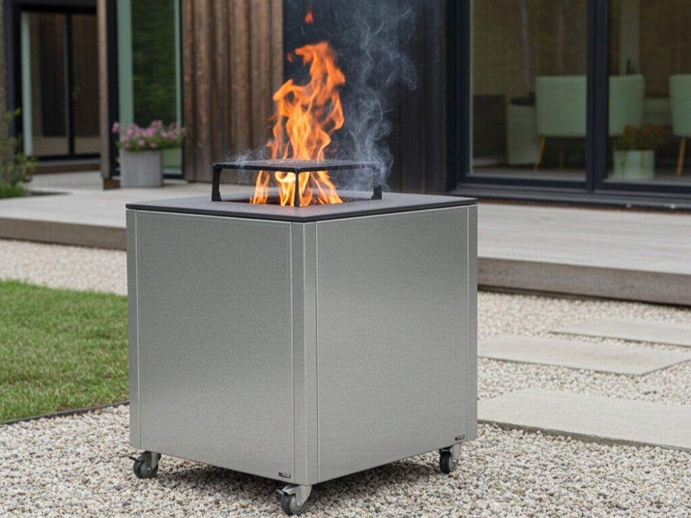 CUBY bålgrill i galvaniseret stål på terrasse ved hus med grøn beplantning og synlige flammer