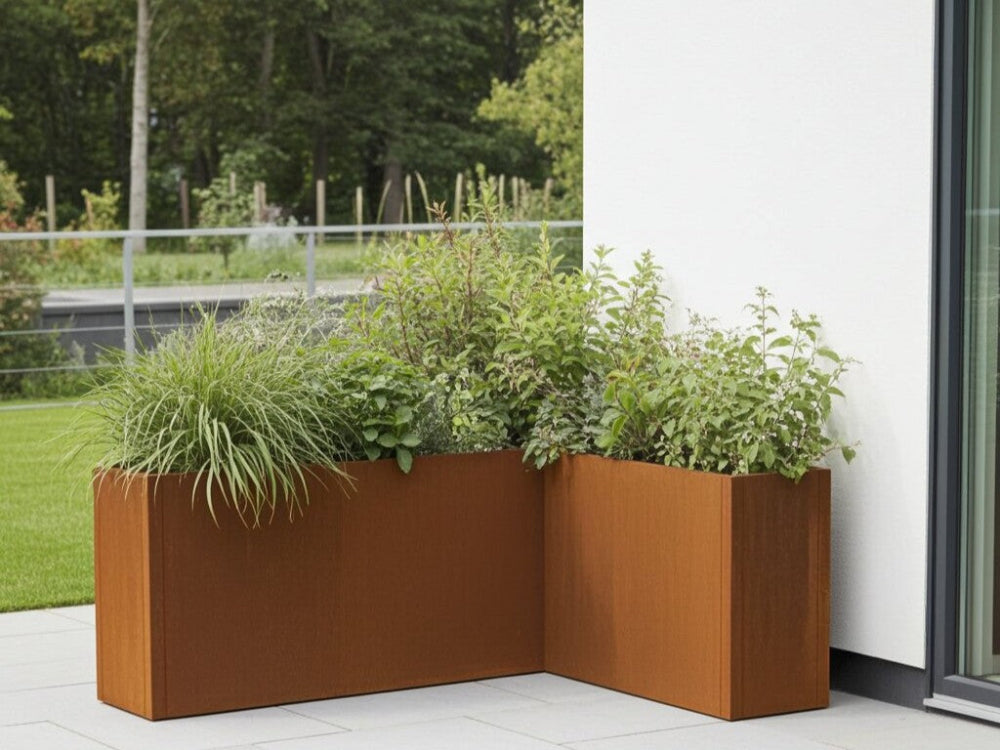 CUBY plantekasse i cortenstål placeret i hjørne med buske og prydgræs ved terrasse