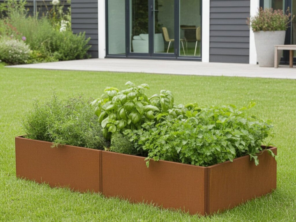 Aflangt EDGY højbed i cortenstål med tæt grøn beplantning foran moderne hus