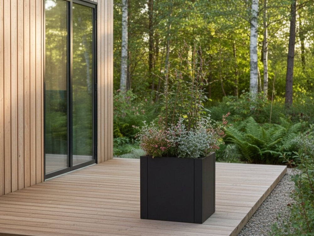 Kvadratisk plantekasse i sort stål med stauder på træterrasse ved moderne bolig