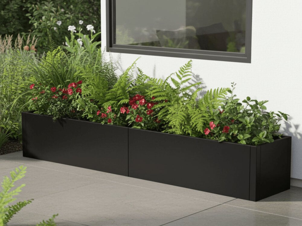 Lang sort plantekasse i stål med bregner og røde blomster ved husfacade