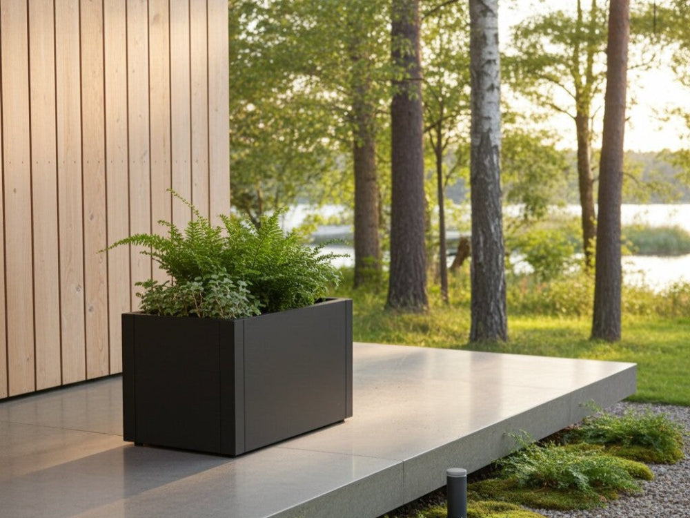 Lav sort plantekasse i stål med bregner ved terrasse og naturgrund