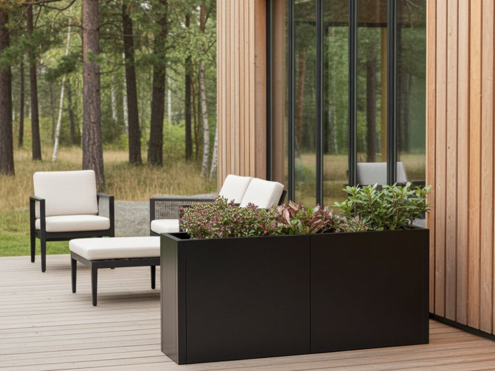 Lang sort plantekasse i stål med stauder ved terrasse og loungemøbler