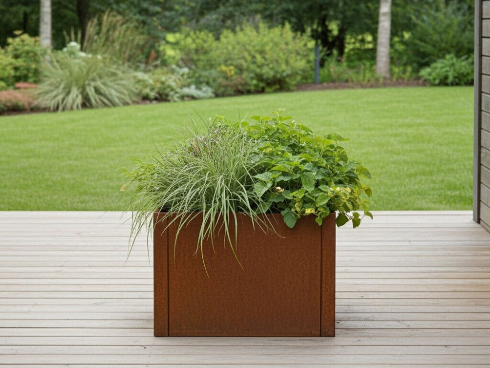 CUBY plantekasse i cortenstål med prydgræsser og grønne planter placeret på træterrasse i moderne have.