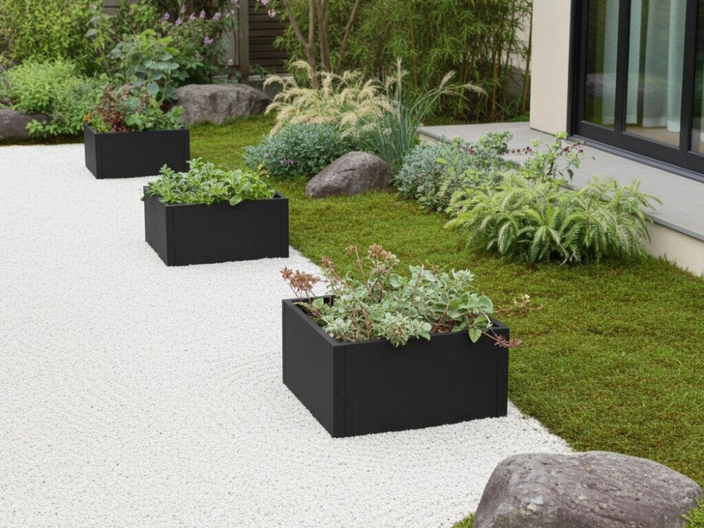 Sorte plantekasser i stål med stauder placeret i minimalistisk have med stenbed