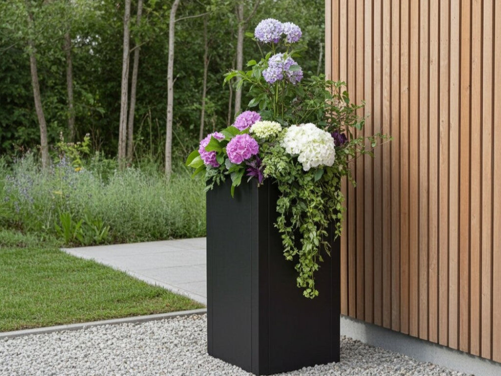 Høj sort plantekrukke i stål med hortensia og hængende planter