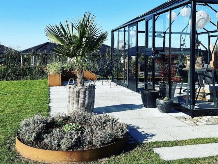 Bedring i cortenstål med planter foran drivhus