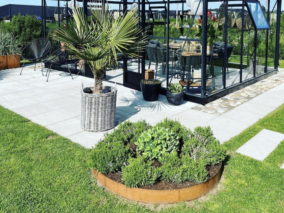 Lav rund bedring i cortenstål med planter ved terrasse og drivhus