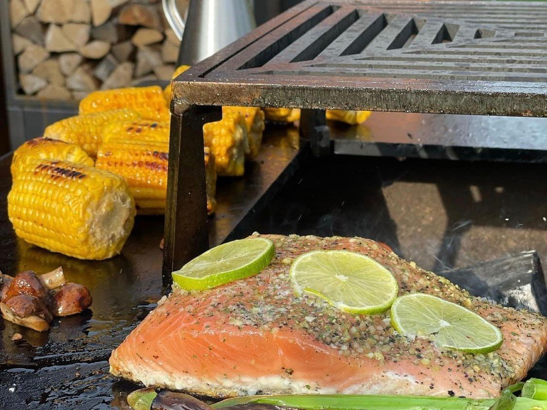 byJEMA bålgrill i cortenstål med sort grillrist – laks med lime, majs og grøntsager tilberedes over åben ild på udendørs stålgrill