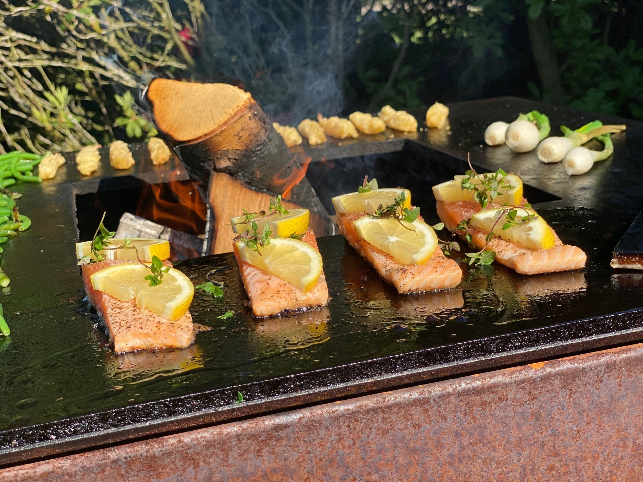 byJEMA bålgrill i cortenstål med sort stegeplade – laksefileter med citron og friske urter tilberedes over åben ild i haven