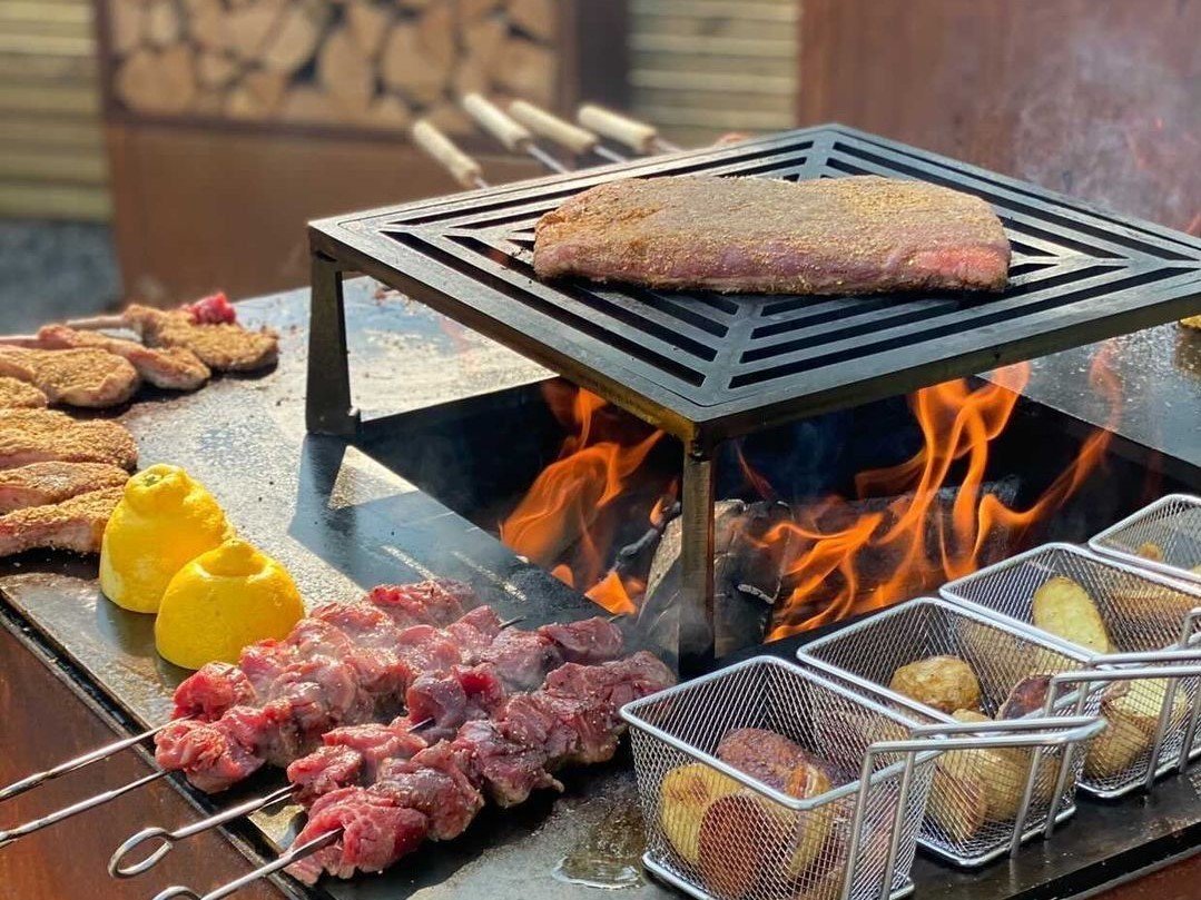 byJEMA bålgrill i cortenstål med sort grillrist – steak, grillspyd og kartofler tilberedes over åben ild med synlige flammer