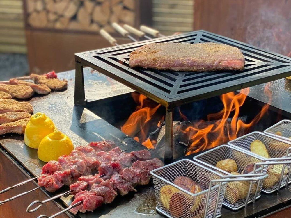 byJEMA bålgrill i cortenstål med sort grillrist – steak, grillspyd og kartofler tilberedes over åben ild med synlige flammer