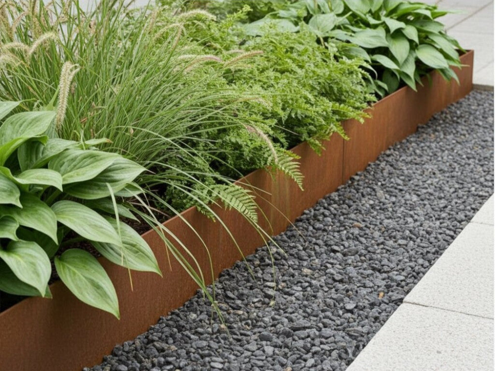 Bedkant i cortenstål med planter og prydgræsser langs grussti i have