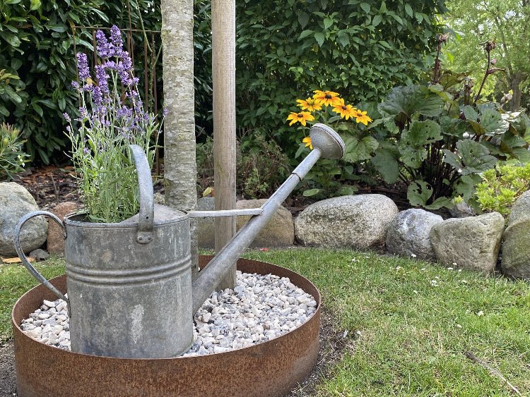 Dekorativ bedring i cortenstål med vandkande og blomster i have