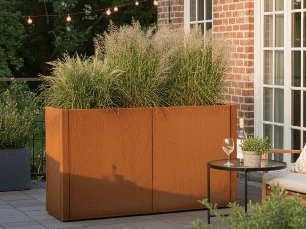 CUBY plantekasse i cortenstål med højt prydgræs på hyggelig terrasse ved murstenshus