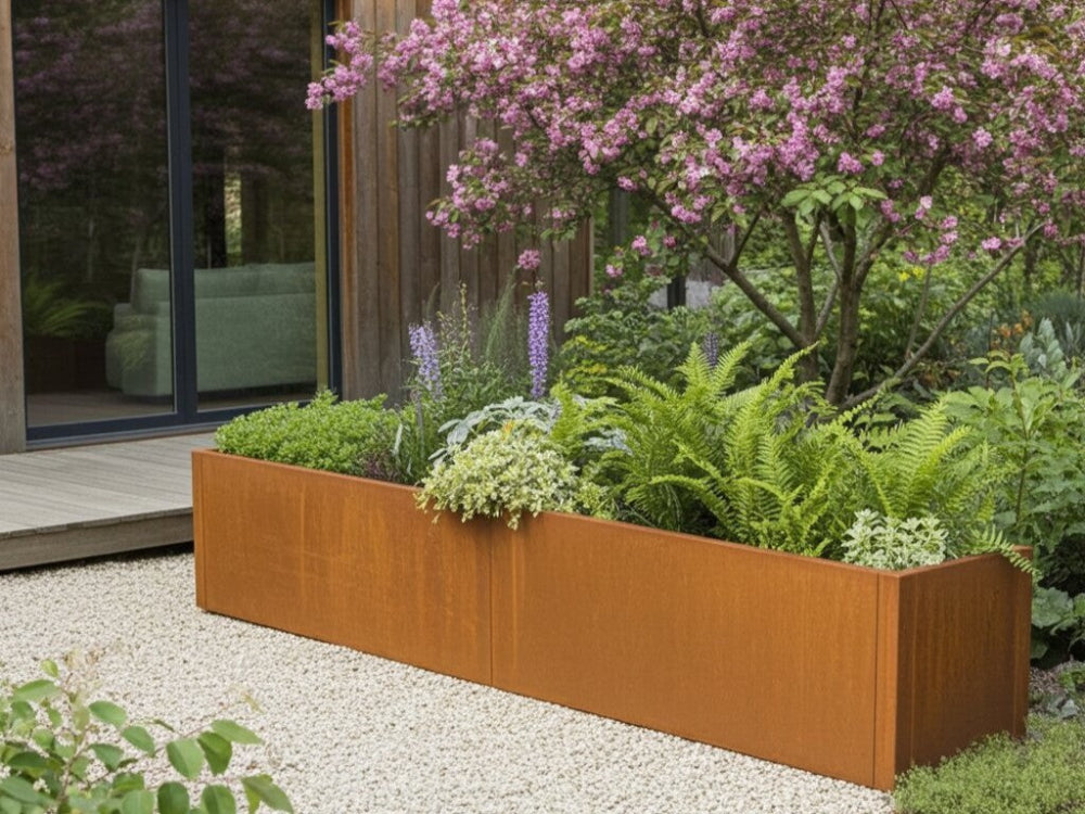 CUBY plantekasse i cortenstål med blomstrende planter under prydtræ i moderne have