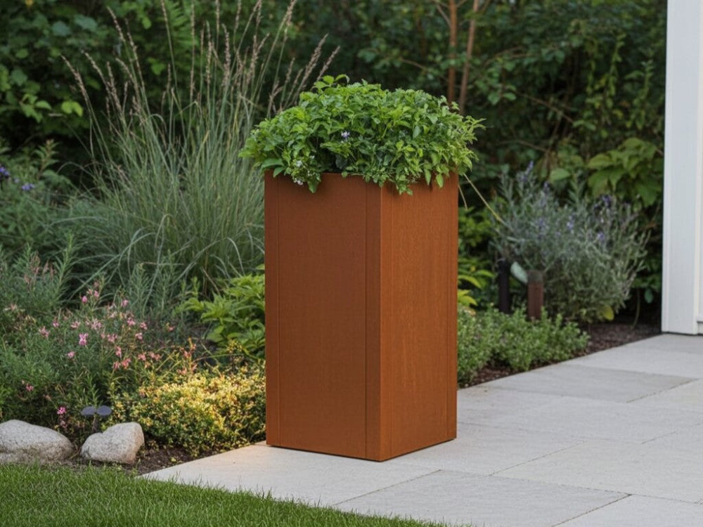 Høj CUBY plantekasse i cortenstål med planter ved havebed