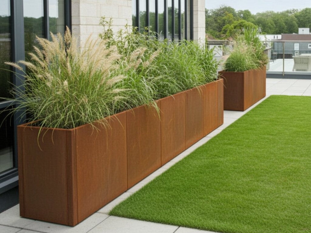 Lang CUBY plantekasse i cortenstål med prydgræs ved moderne bygning