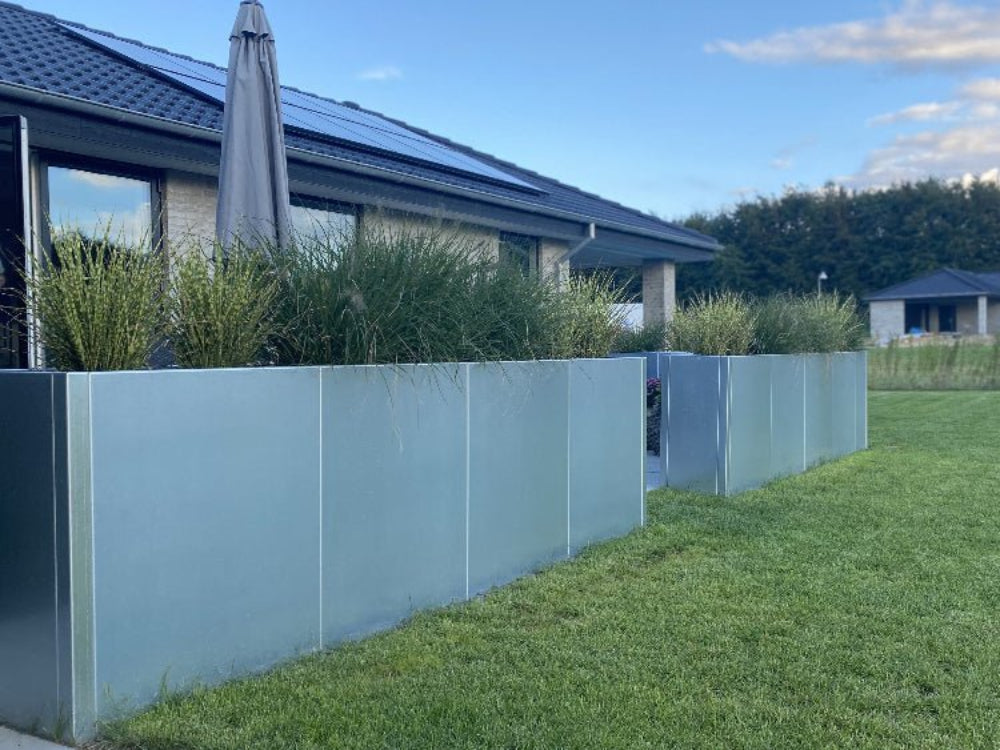 Flere CUBY aflange plantekasser i galvaniseret stål opstillet som afgrænsning i have