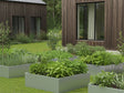 Flere højbed i galvaniseret stål med planter og urter i moderne villahave ved træfacade