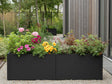 Lang sort plantekasse i stål med blomstrende planter i moderne have