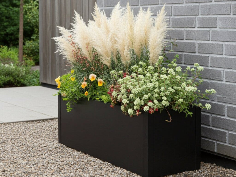 Sort plantekasse i stål med pampasgræs og blomstrende planter