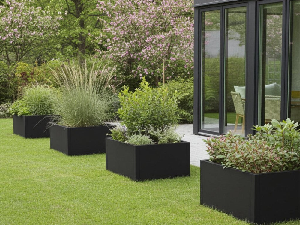 Sorte plantekasser i stål med grønne planter placeret som afgrænsning langs terrasse