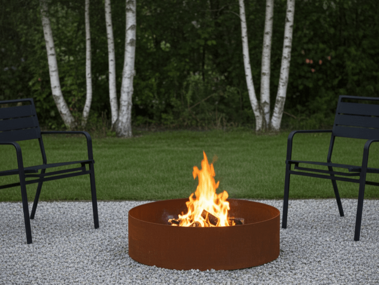 Rundt bålfad i cortenstål placeret på grus mellem to havestole i haven