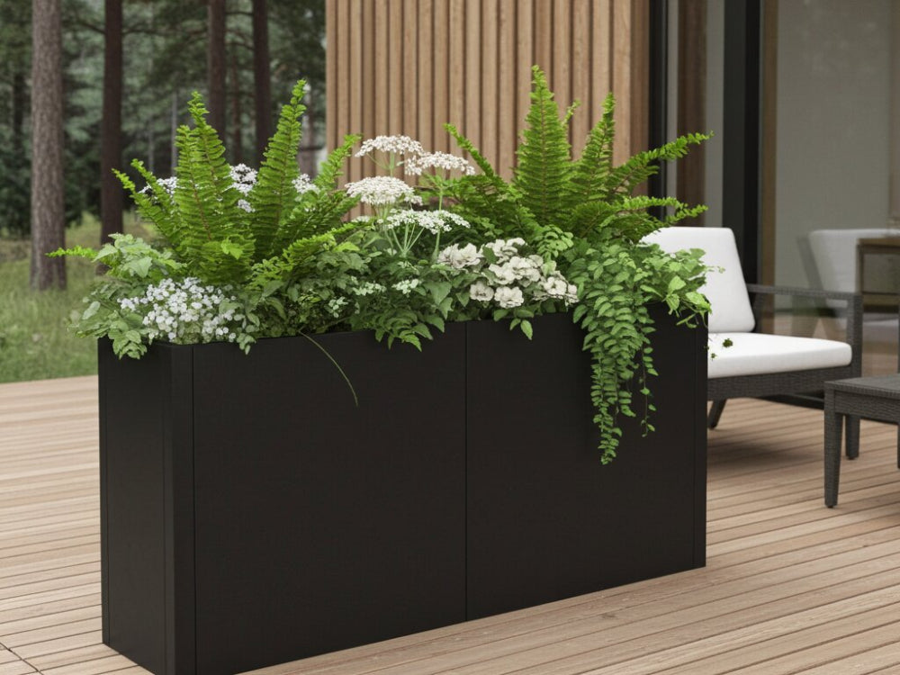 Sort plantekasse i stål med bregner og hvide blomster på træterrasse