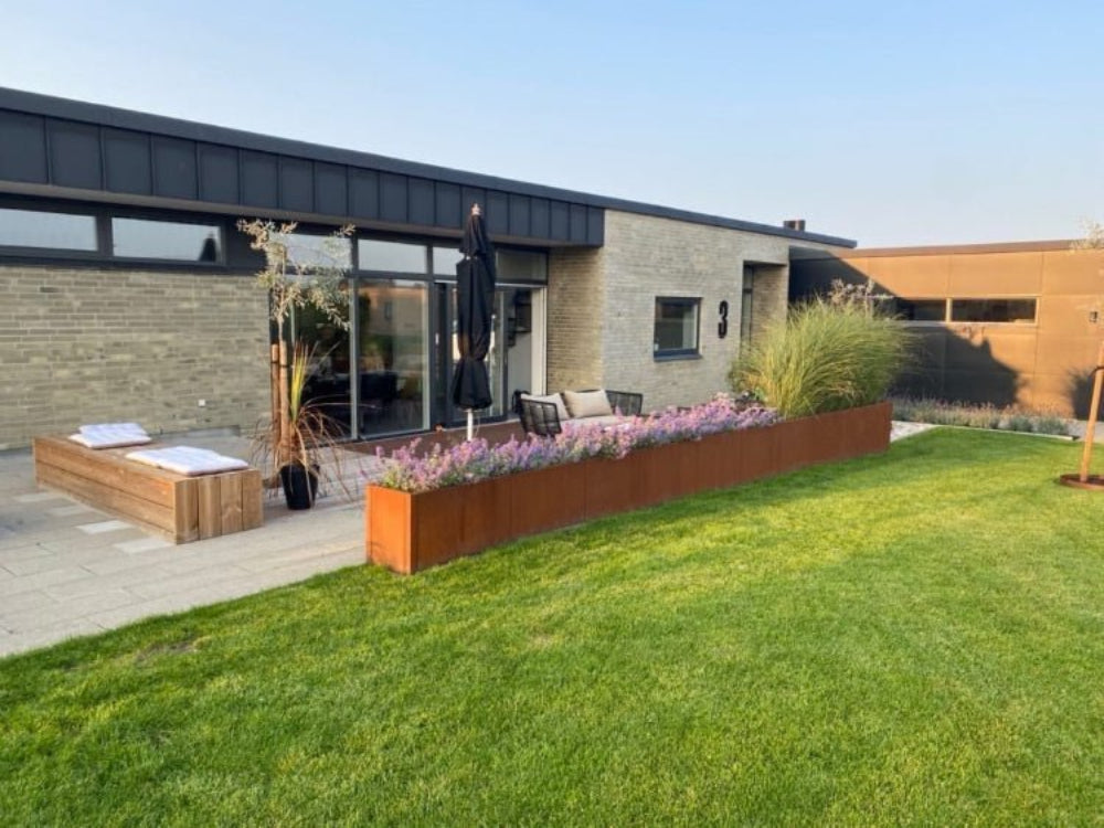 Lang CUBY plantekasse i cortenstål med blomster foran moderne hus