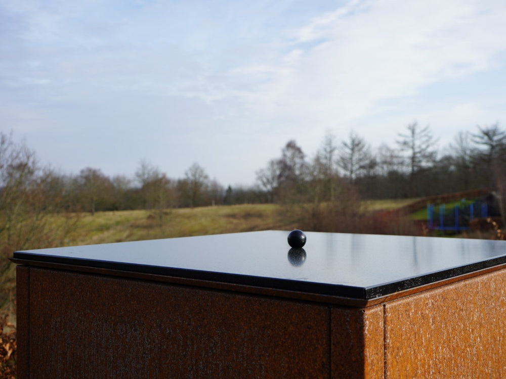 Låg i sortlakeret stål med blank overflade i naturligt dagslys